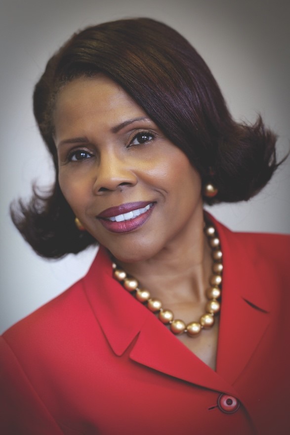 Portrait of Belinda Moore wearing a red blazer and a pearl necklace