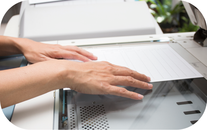 Hands placing a sheet of paper on a photocopier or scanner.