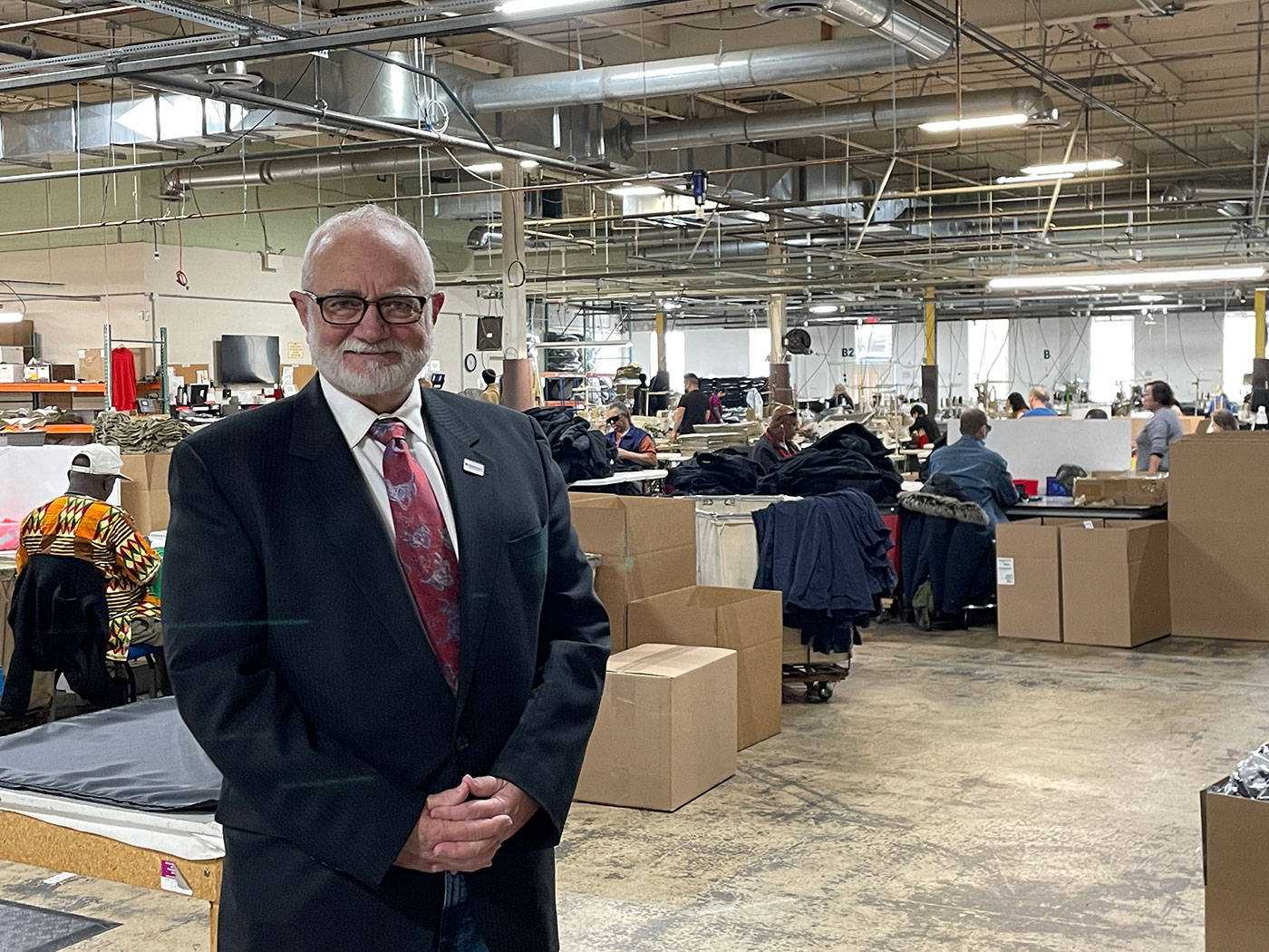 Bestwork Industries for the Blind training facility, man in a suit standing in a warehouse with workers and boxes