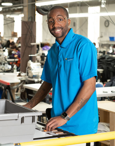 Bestwork Industries for the Blind training facility, worker polo shirt smiling while using a workstation with sewing machines