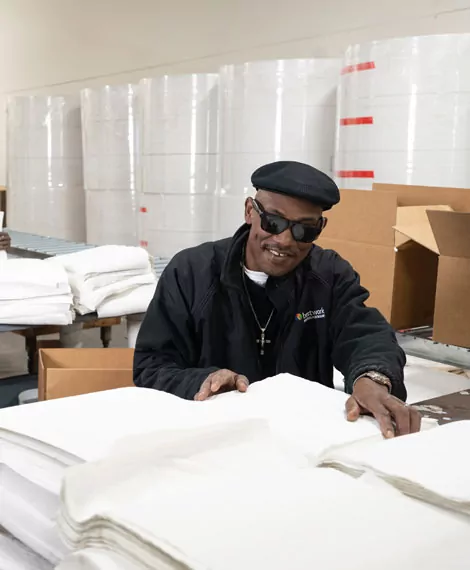 Man with black hat, glasses and jacket organizing sheets of paper in four piles Bestwork industries for the blind factory