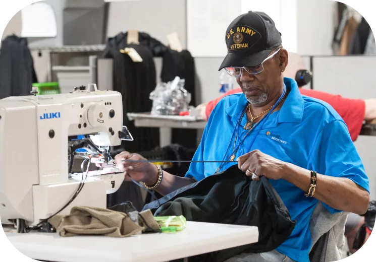 Man wearing a black U.S. Army Veteran hat, wearing a blue Bestwork shirt, operating a sewing machine