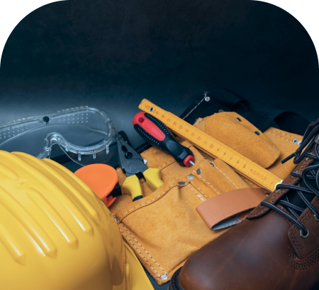 Construction tools and safety gear including a yellow hard hat, safety goggles, pliers, a ruler, and a brown work boot