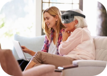 Two women sitting on a couch, one wearing a visor and looking at a laptop, the other smiling and engaged