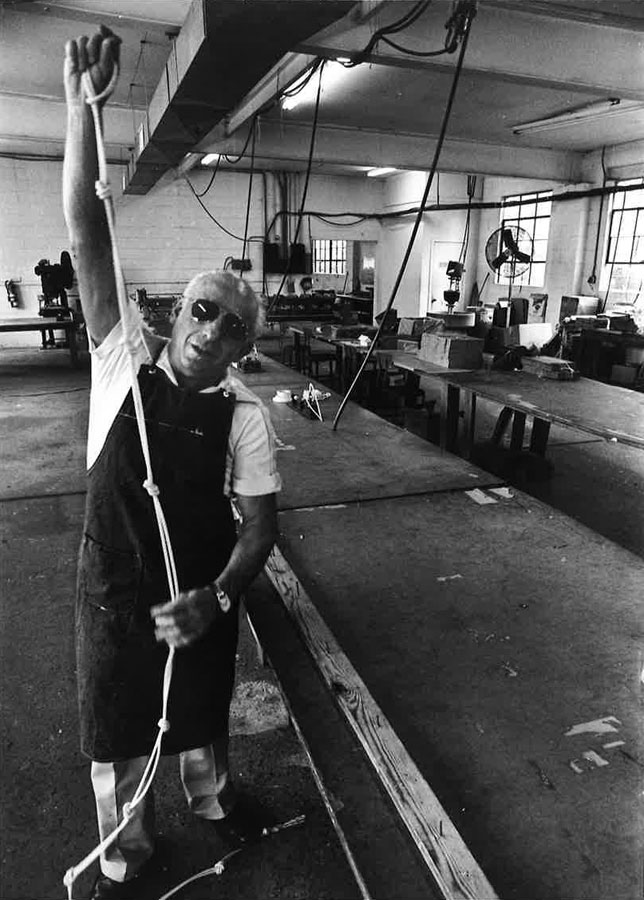 A man wearing sunglasses demonstrates a rope in a workshop with tables and equipment