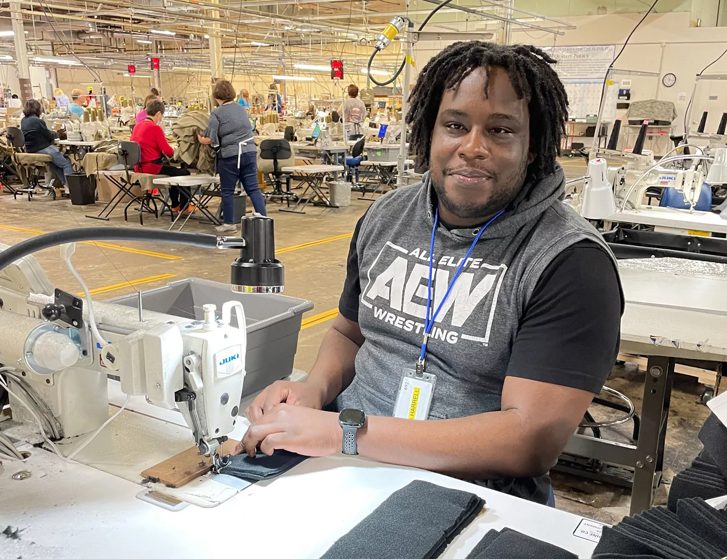 Man with black t-shirt and gray pullover hoodie sewing while smiling for the camera 