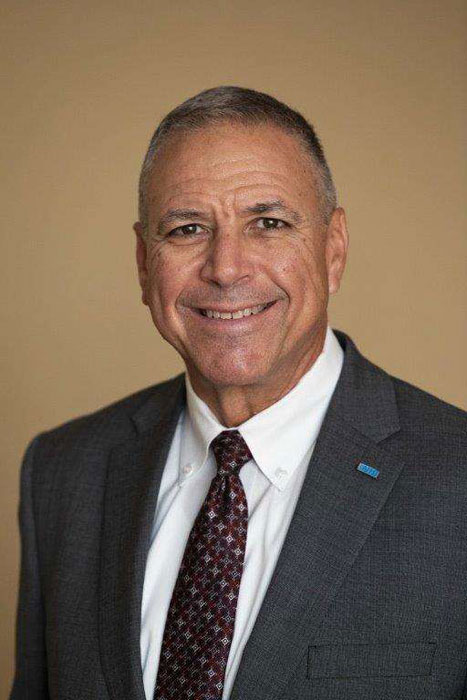 Man in a suit with a tie, smiling against a neutral background