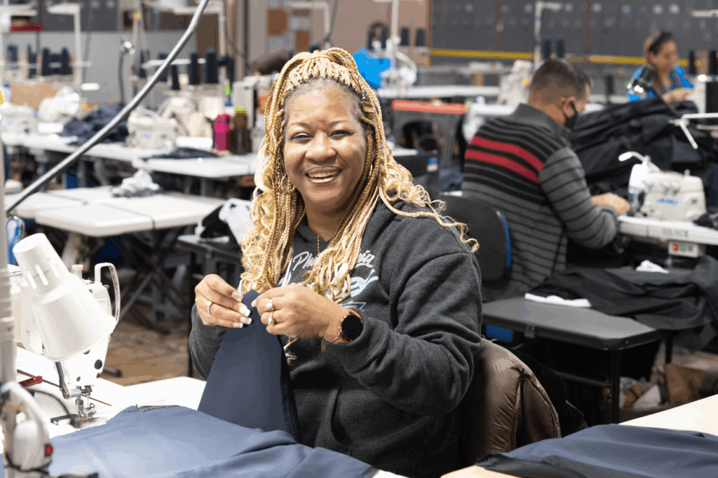Bestwork Industries for the Blind training facility, woman smiling while sewing, other workers in background at sewing machines.