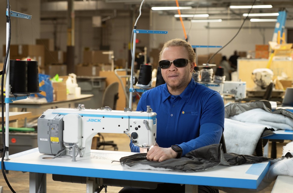 Training facility for individuals with visual impairments, workers using sewing machines, focus on textile production.