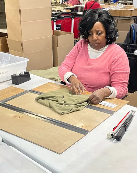 Woman in a pink sweater folding a shirt in a Bestwork industries for the blind factory