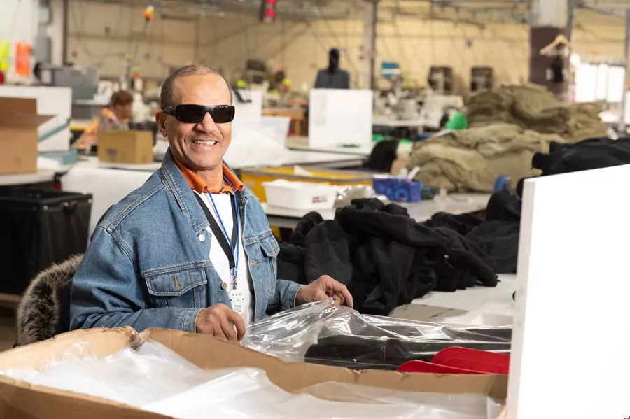 Man smiling, wearing a blue jean jacket, packaging materials at a Bestwork factory