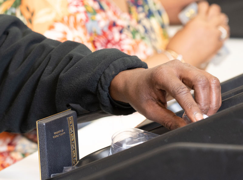 Close up of two people sitting near eachother, one hand reaching for a small item at a counter
