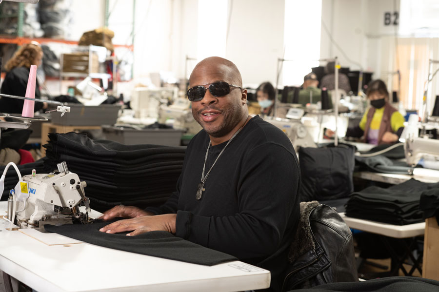 Sewing workshop with a man wearing sunglasses at a sewing machine, surrounded by fabric and other workers